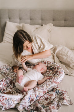 Woman playing with a baby on a floral baby nest or baby lounger in a bedroom setting