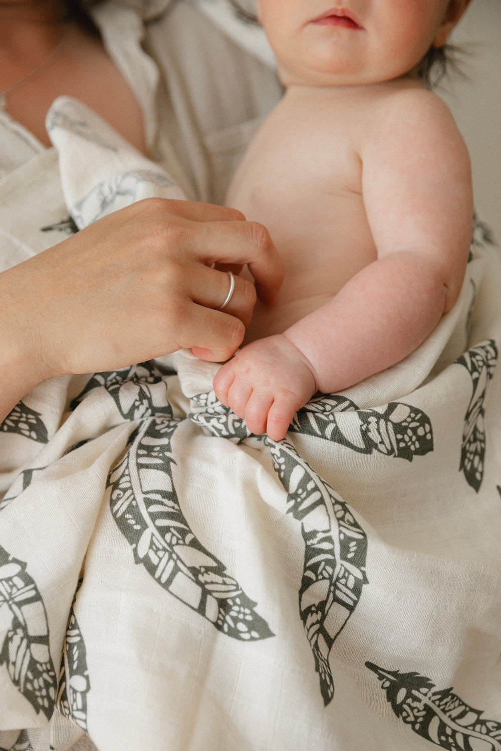 a baby in feather pattern cotton wrap being held by adult 