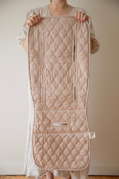 A person holding up a neutral organic cotton pram liner with both hands  in front of them 