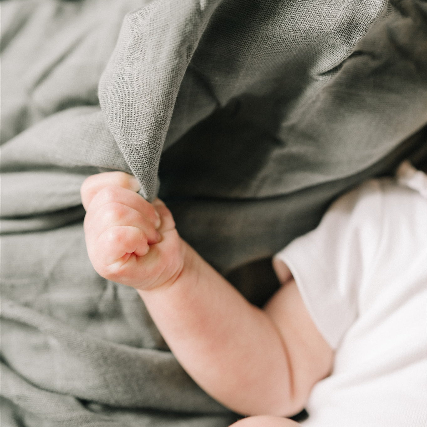 a baby in white clothes laying on a green swaddle holding the fabric in its hand 